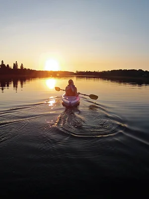 A woman paddles a kayak into the sunset in Sioux Narrows
